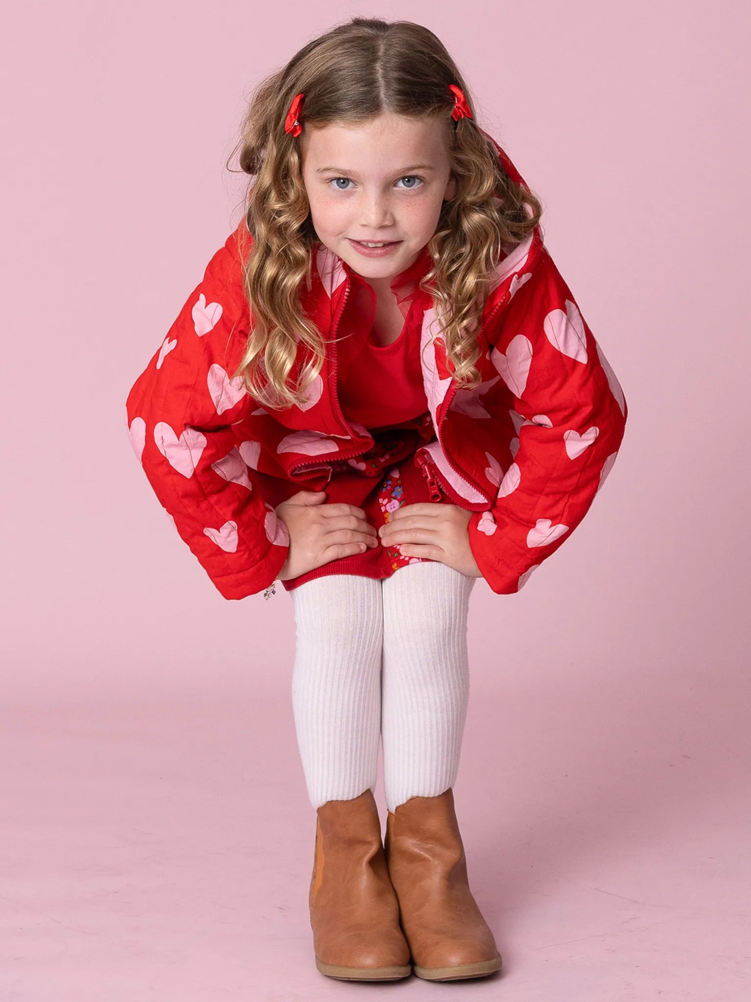 Young girl wearing a red jacket with heart patterns on a pink background