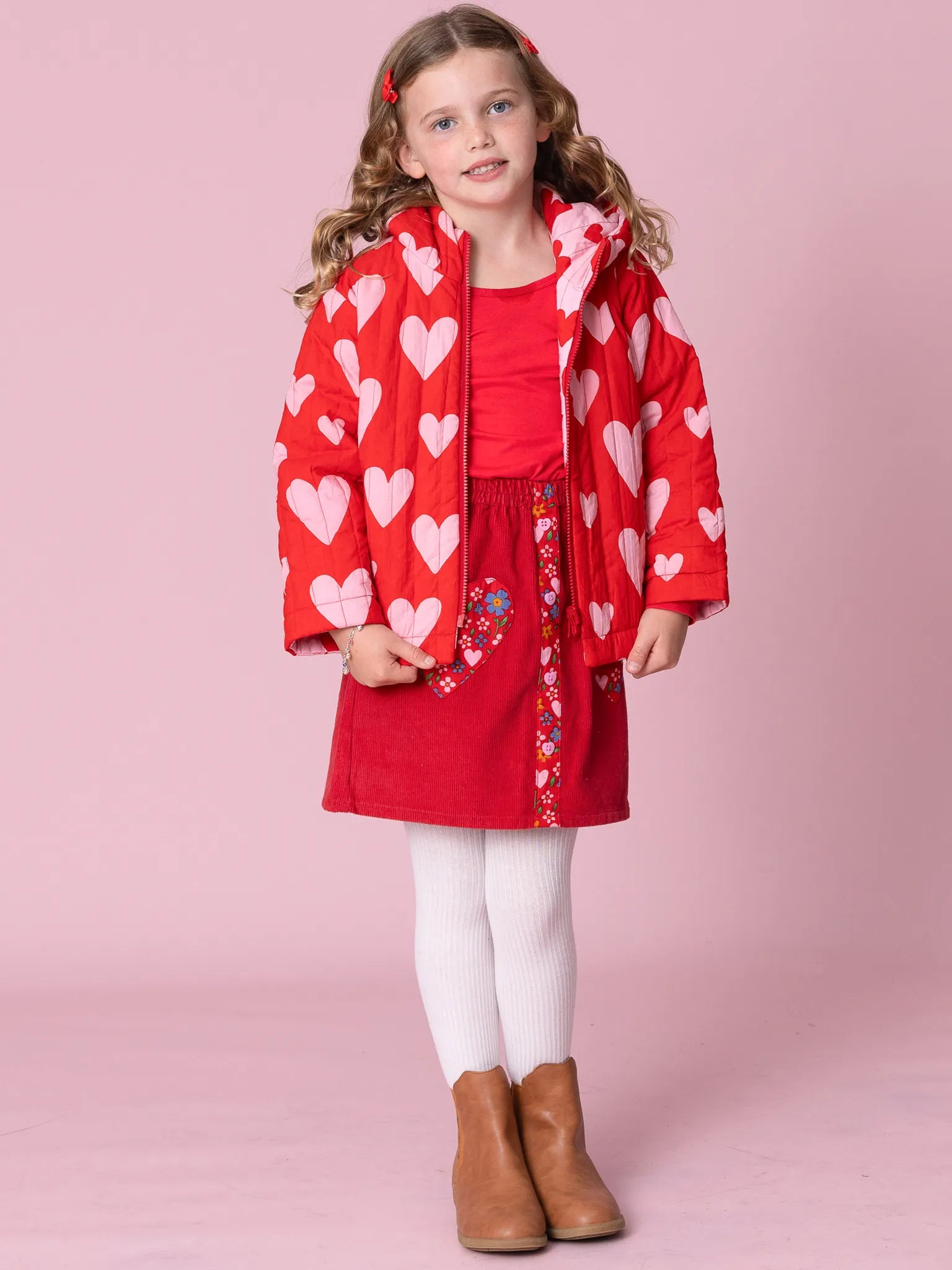 Young girl wearing a red heart-patterned coat on a pink background