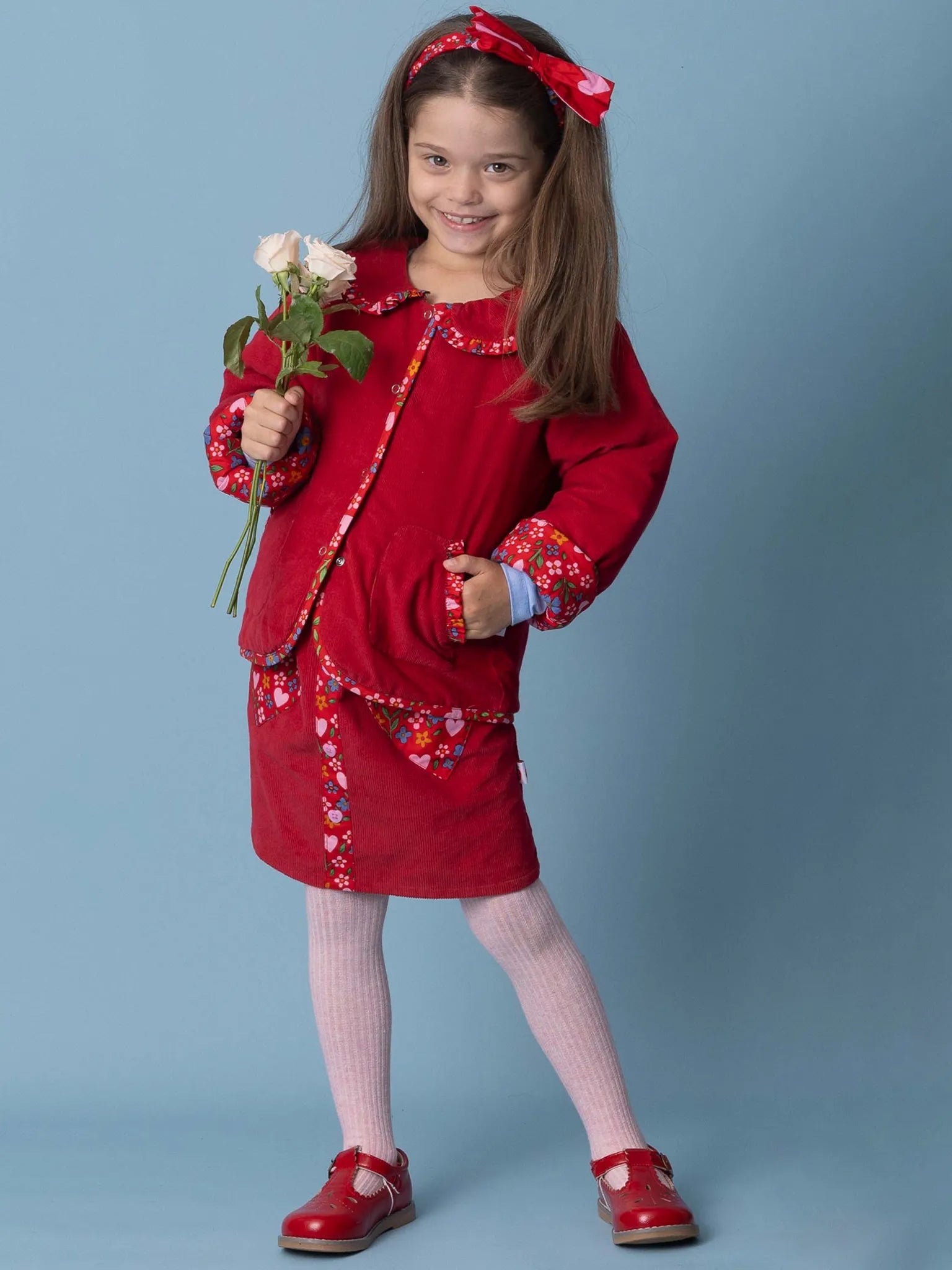 Young girl in a red outfit with floral patterns holding a flower against a blue background