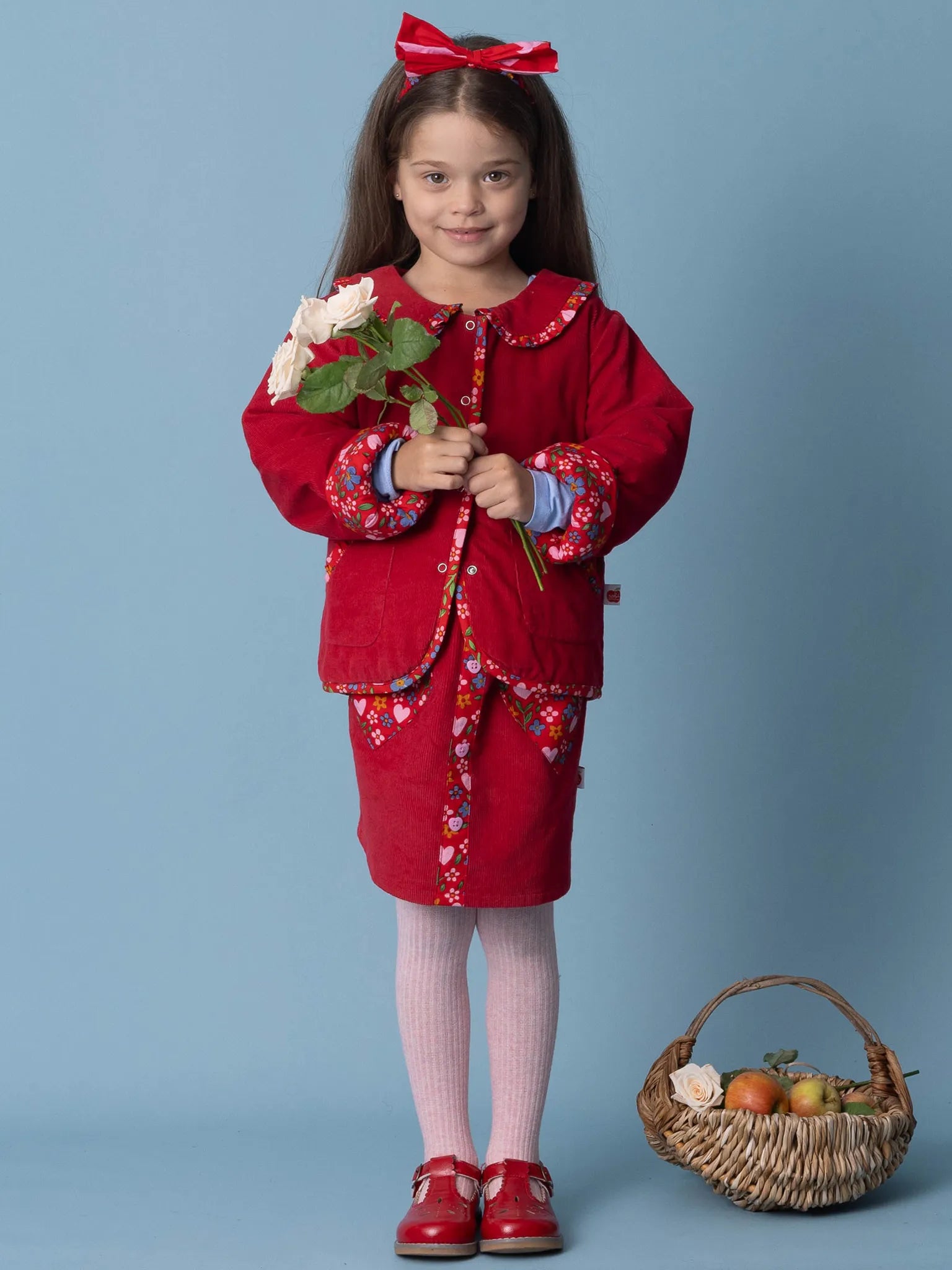 Young girl in a red outfit holding flowers against a blue background