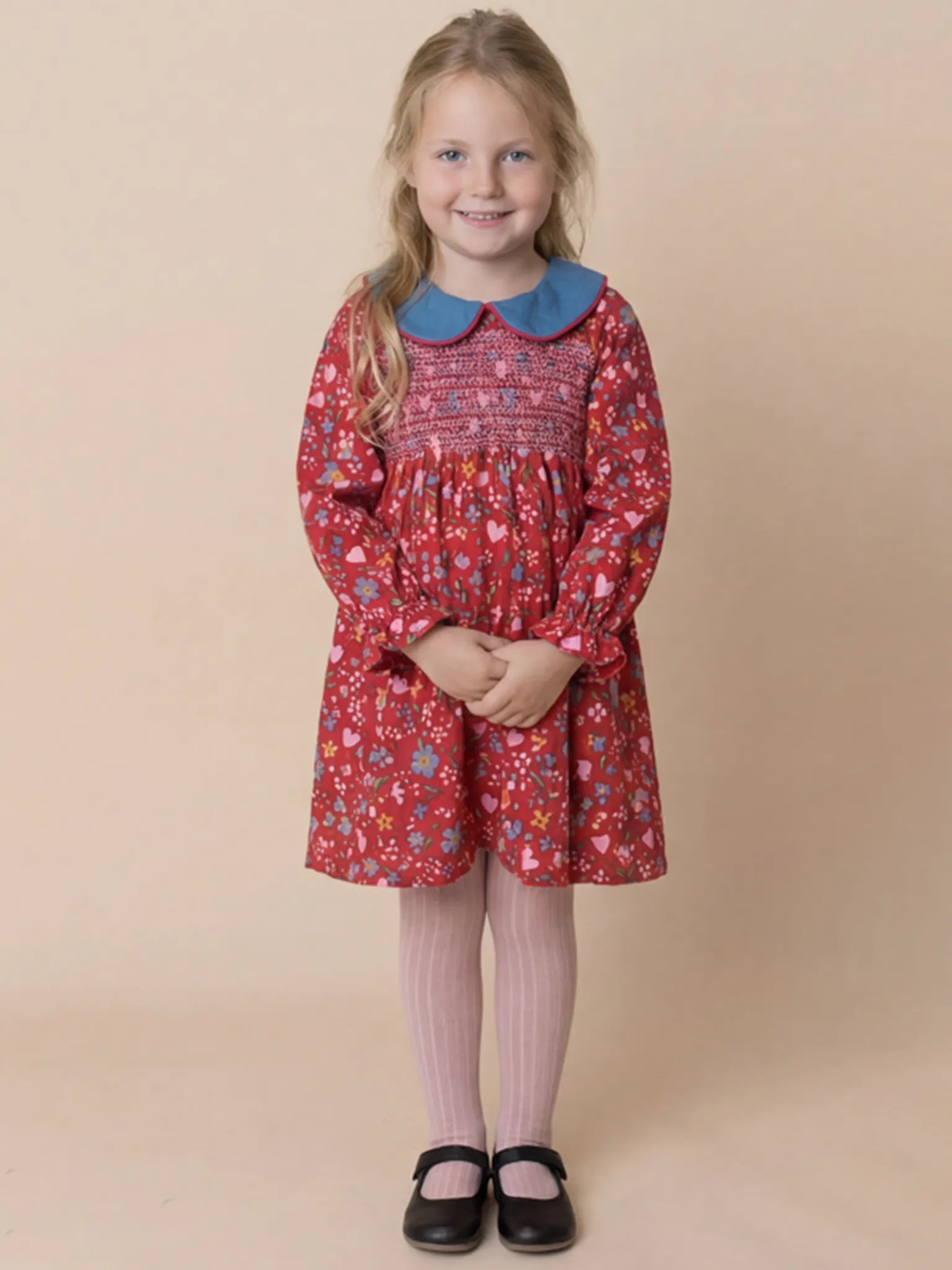 Young girl wearing a red floral dress with a blue collar on a beige background