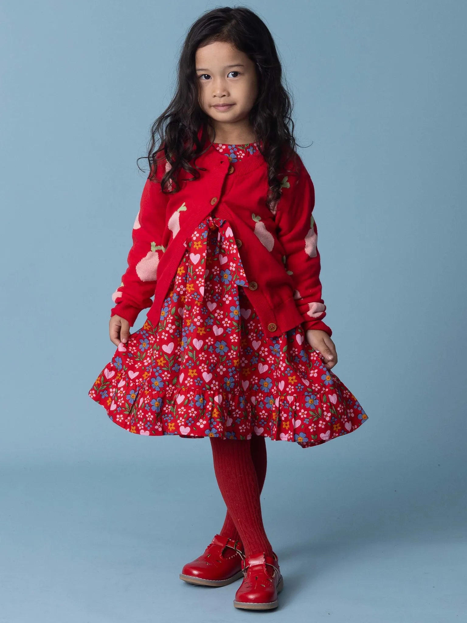 Young girl wearing a red outfit with a floral dress on a blue background