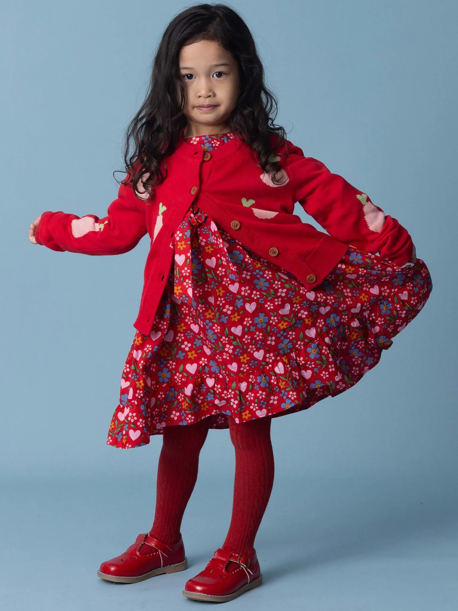 Young girl wearing a red coat over a floral dress on a blue background