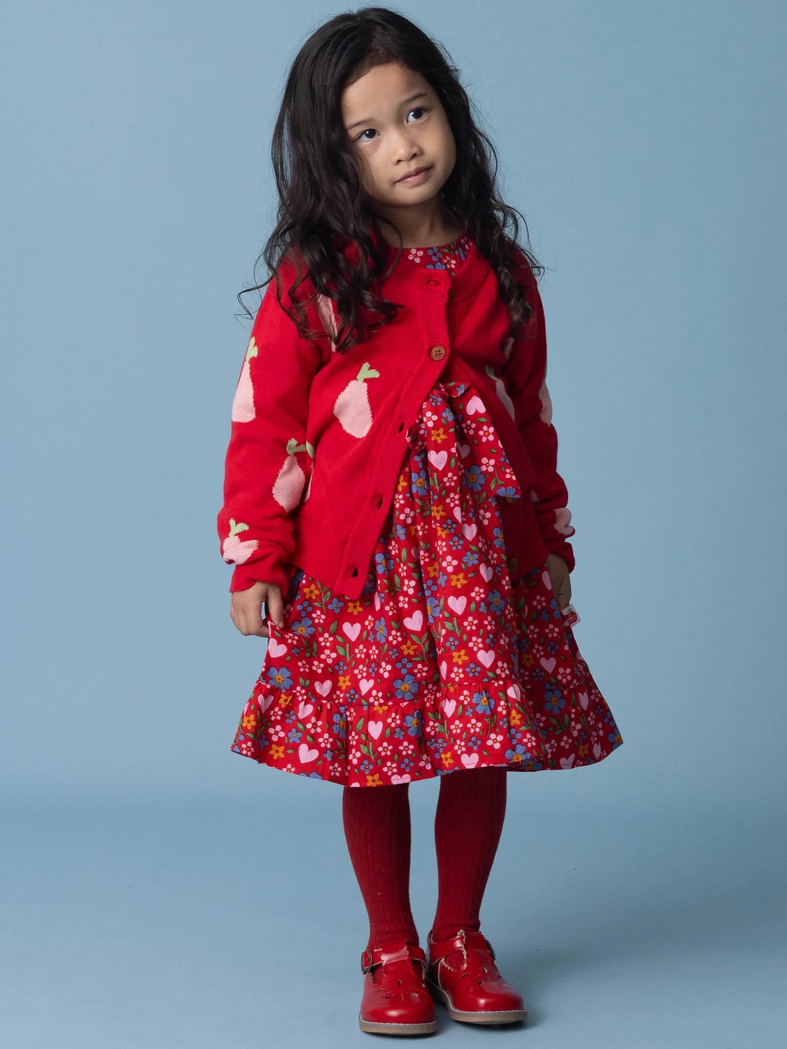 Young girl wearing a red coat and dress with heart patterns on a blue background