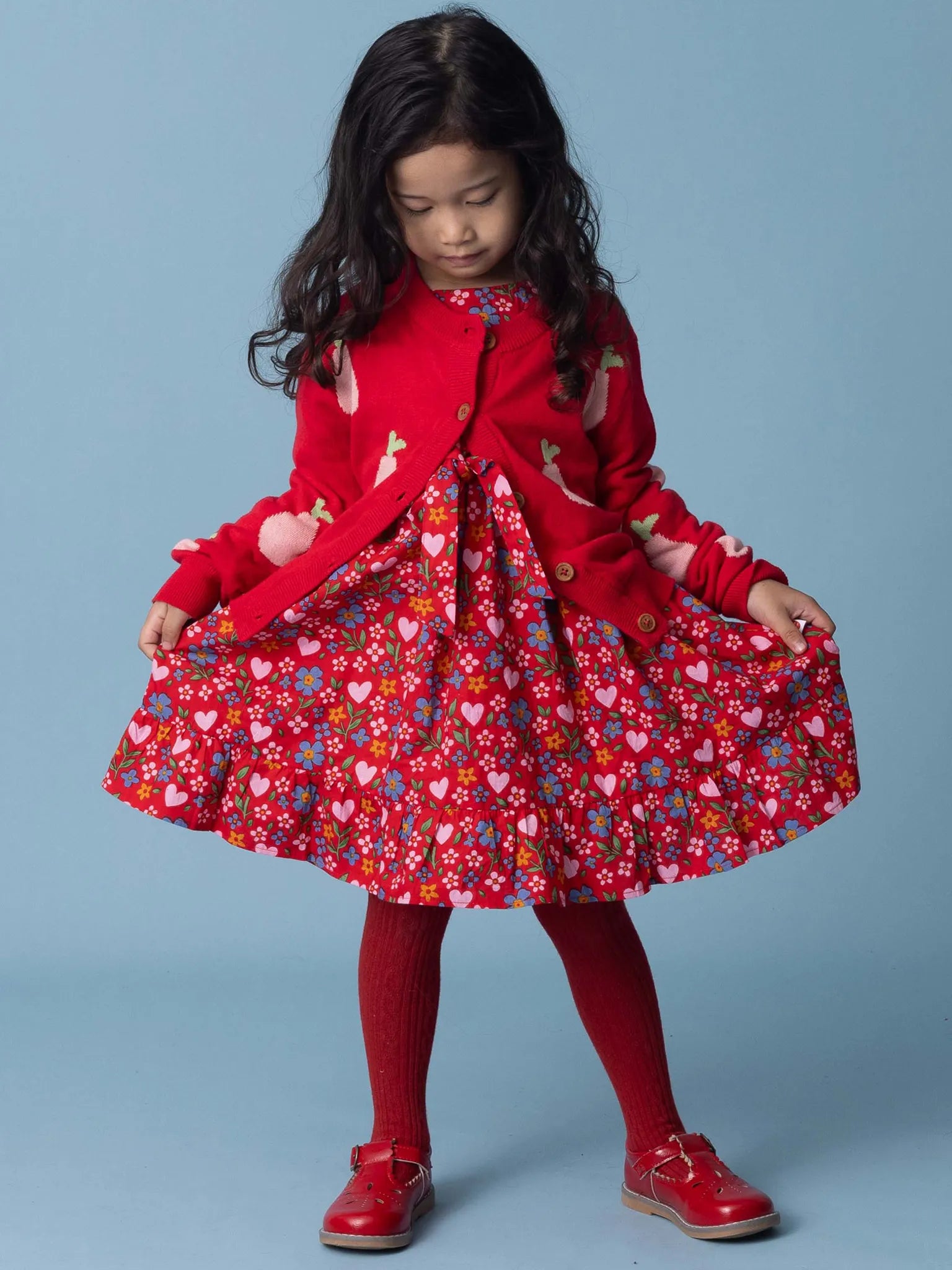 Young girl wearing a red dress with a floral pattern and a matching red coat on a blue background