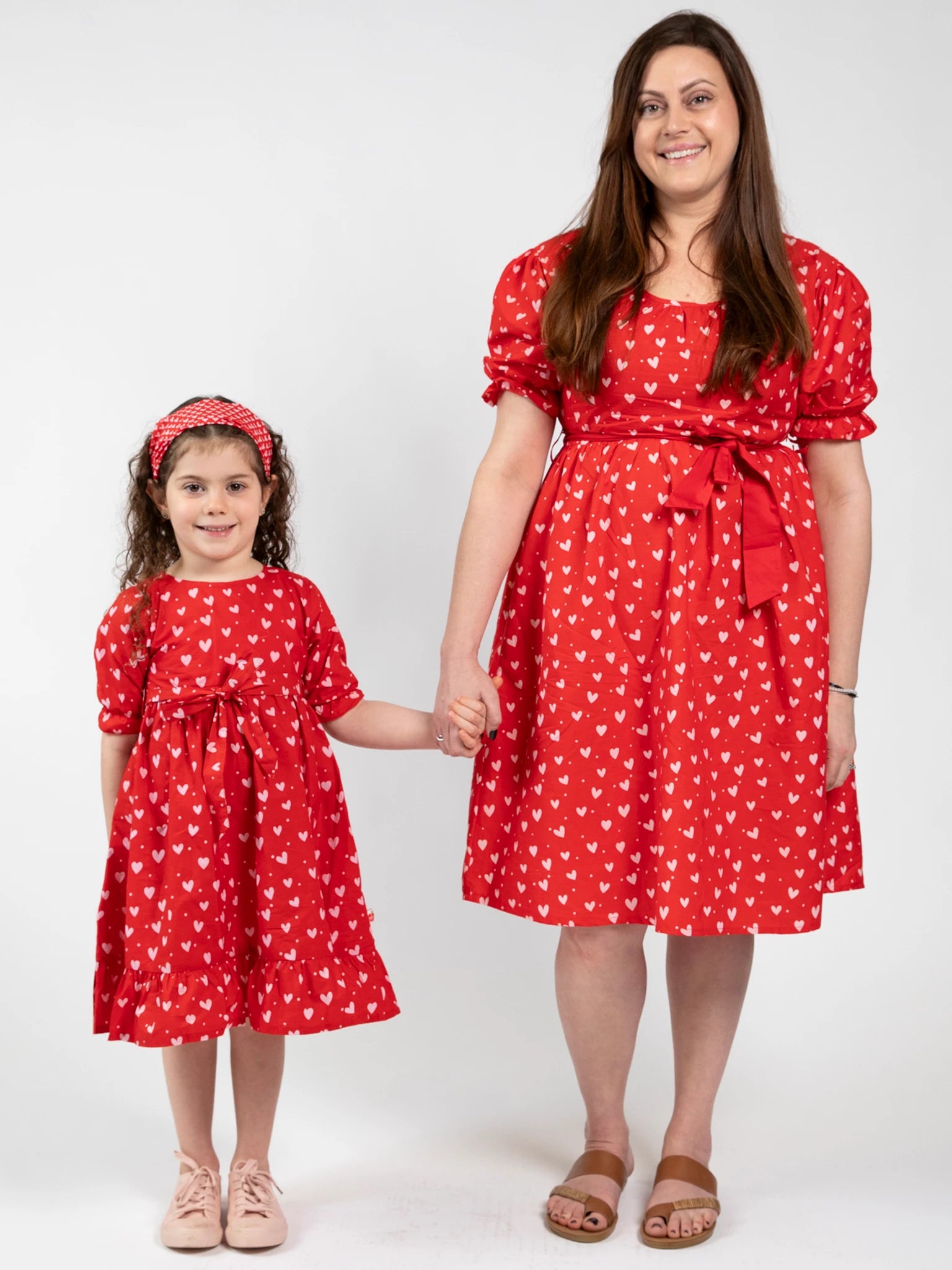 A woman and a young girl wear matching Hearts Red & Pink Heart Midi Dresses, standing hand-in-hand against a plain white background.