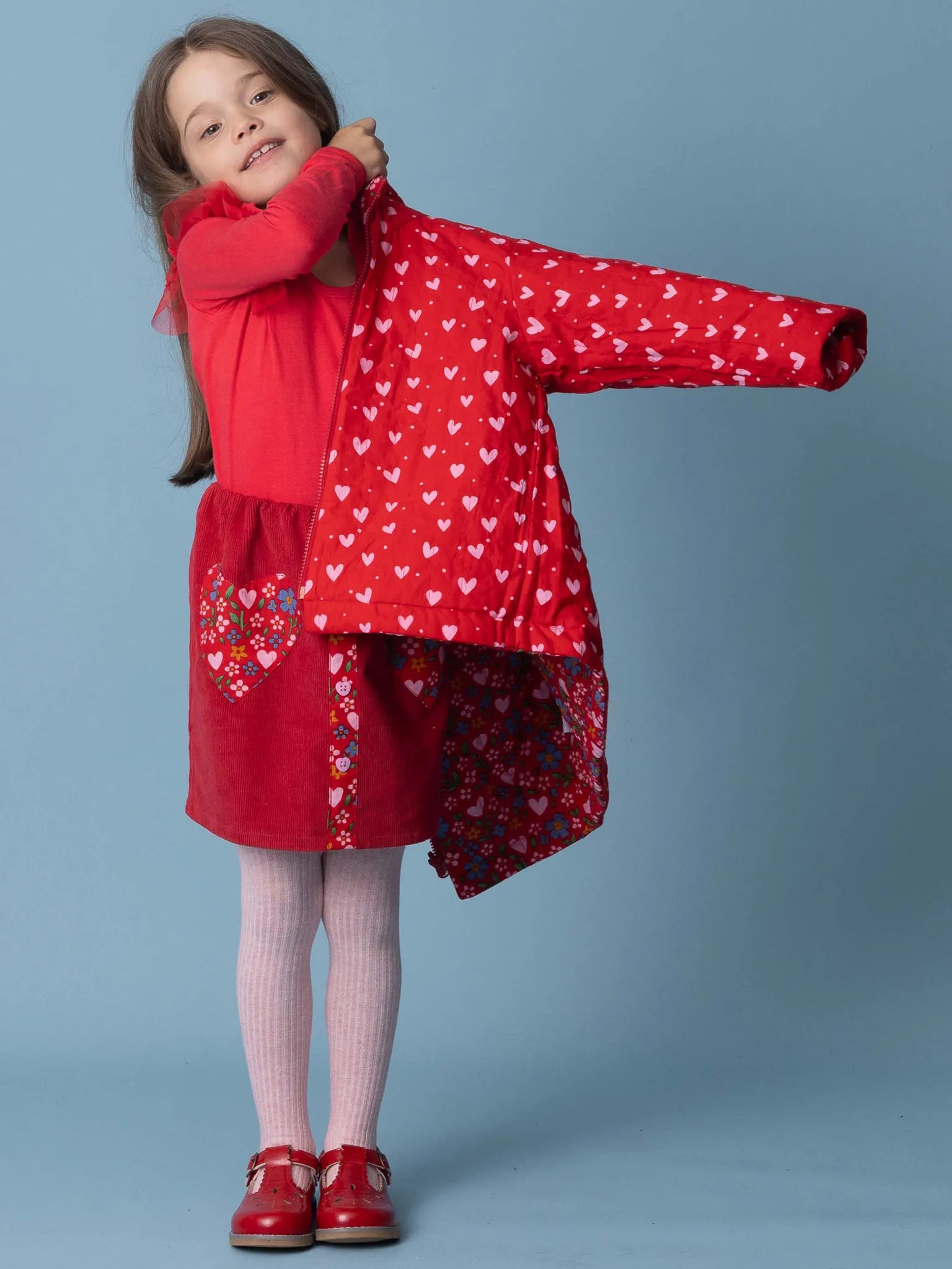 Young girl wearing a red dress with heart patterns against a blue background