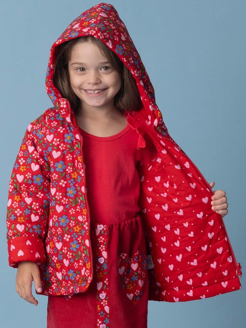 Child wearing a red floral-patterned jacket against a blue background