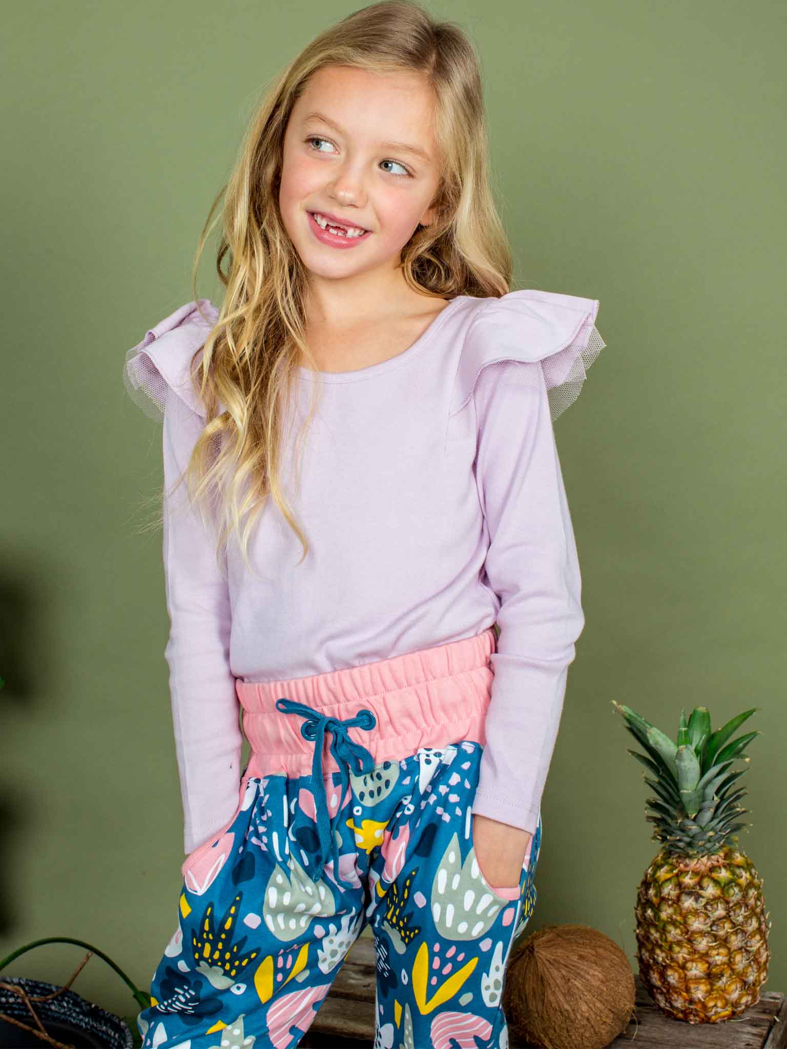 Young girl wearing a light purple top and colorful pants with a green background