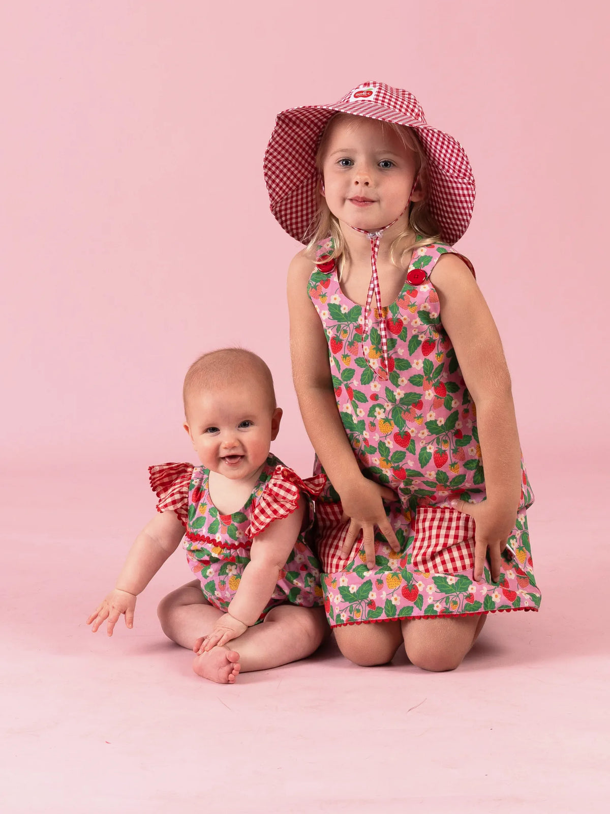 Girl in the Strawberry Fields Gracie dress kneeling beside a baby in the Strawberry Fields romper