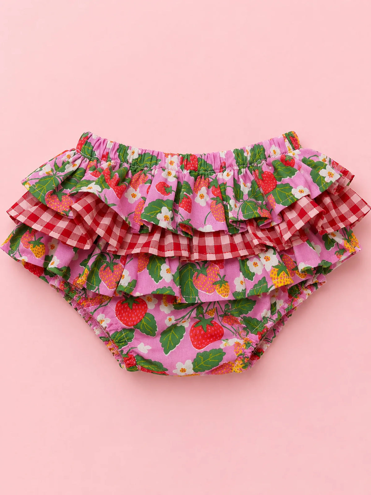 Pink ruffled diaper cover featuring a strawberry and leaf print, red gingham check, and white daisy details, laid flat on a solid pink background.