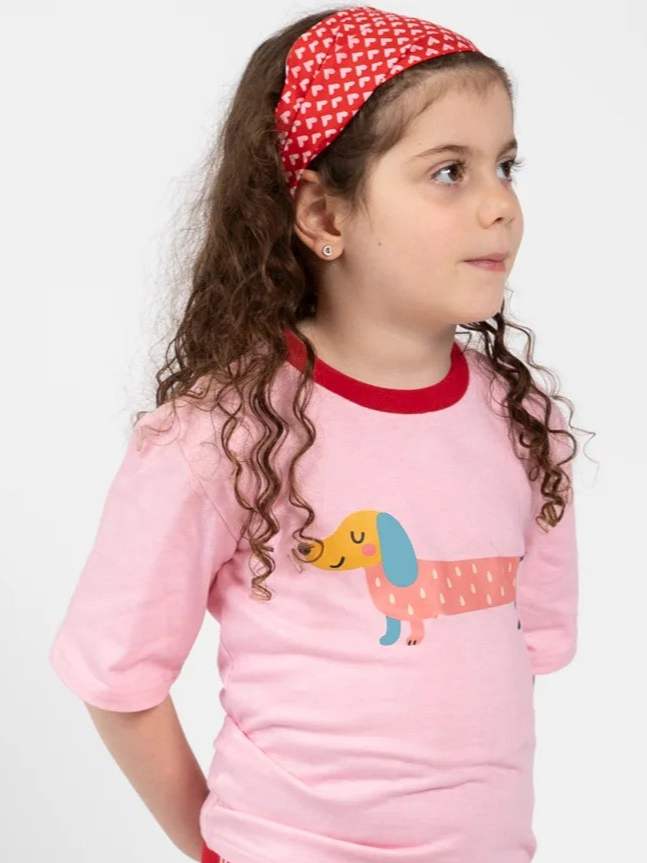 A young child with long curly hair wears the Essentials Red and Pink Hearts Headband and a pink T-shirt with a cartoon dachshund, looking to the side against a plain background.