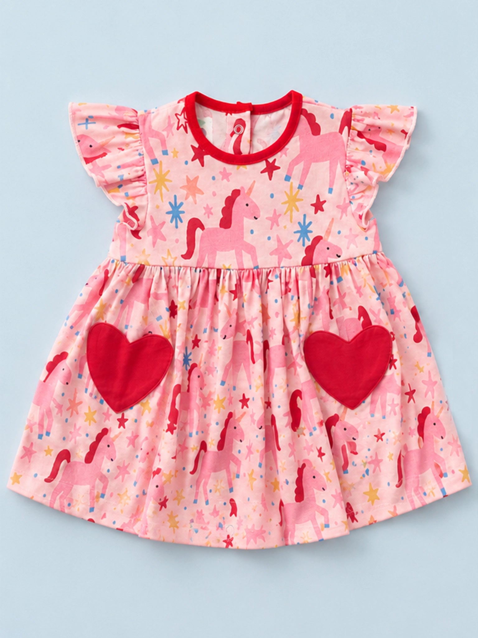 A pink children's dress with a unicorn and star print, featuring red ruffle sleeves, a red crew neck, and two large red heart pockets on the skirt, shown against a light blue background.