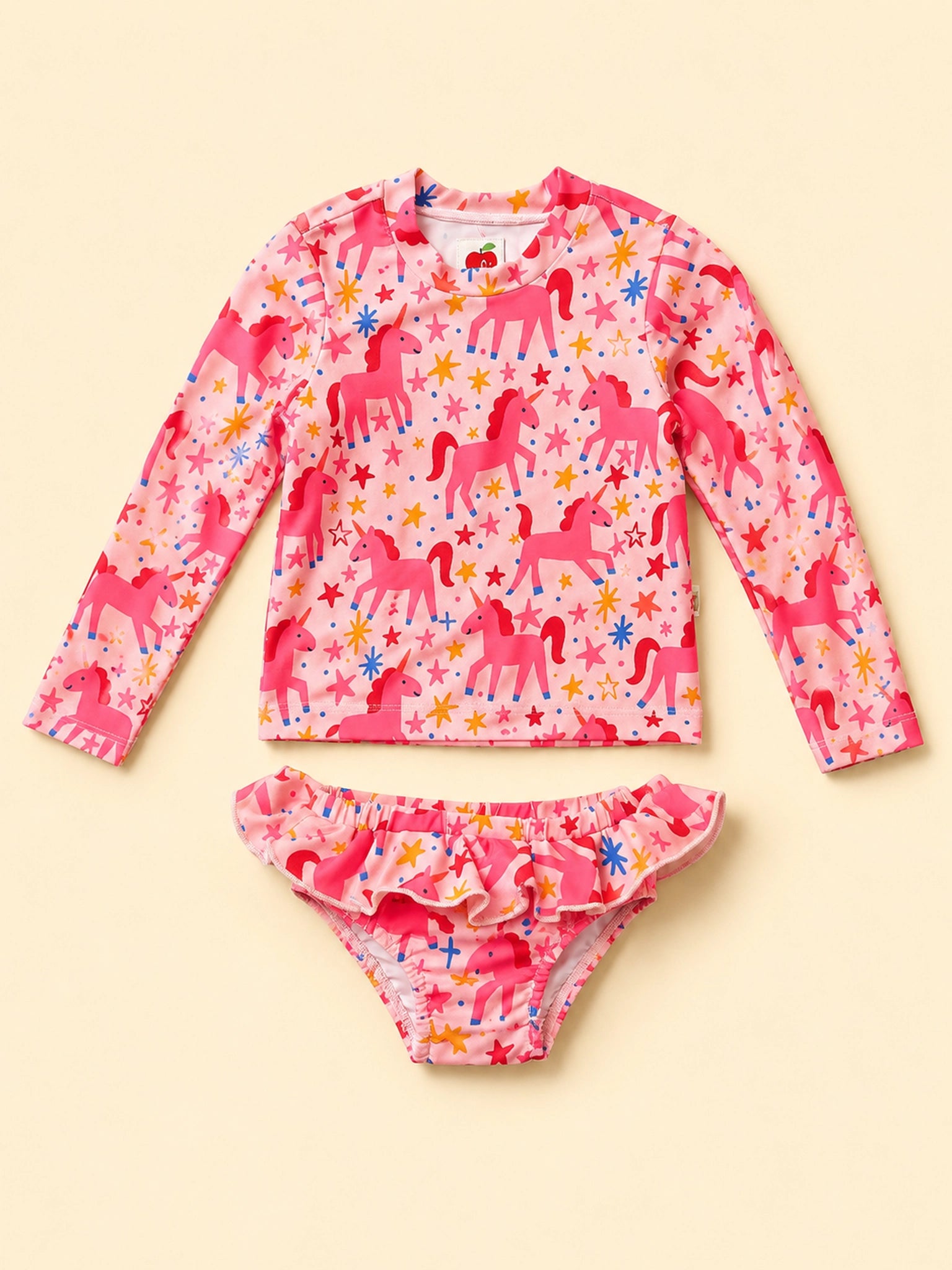 A two-piece girls' swim set featuring a long-sleeve rash guard and matching ruffled bikini bottoms, both in a pink unicorn pattern on a light pink background, laid flat on a cream-colored background.