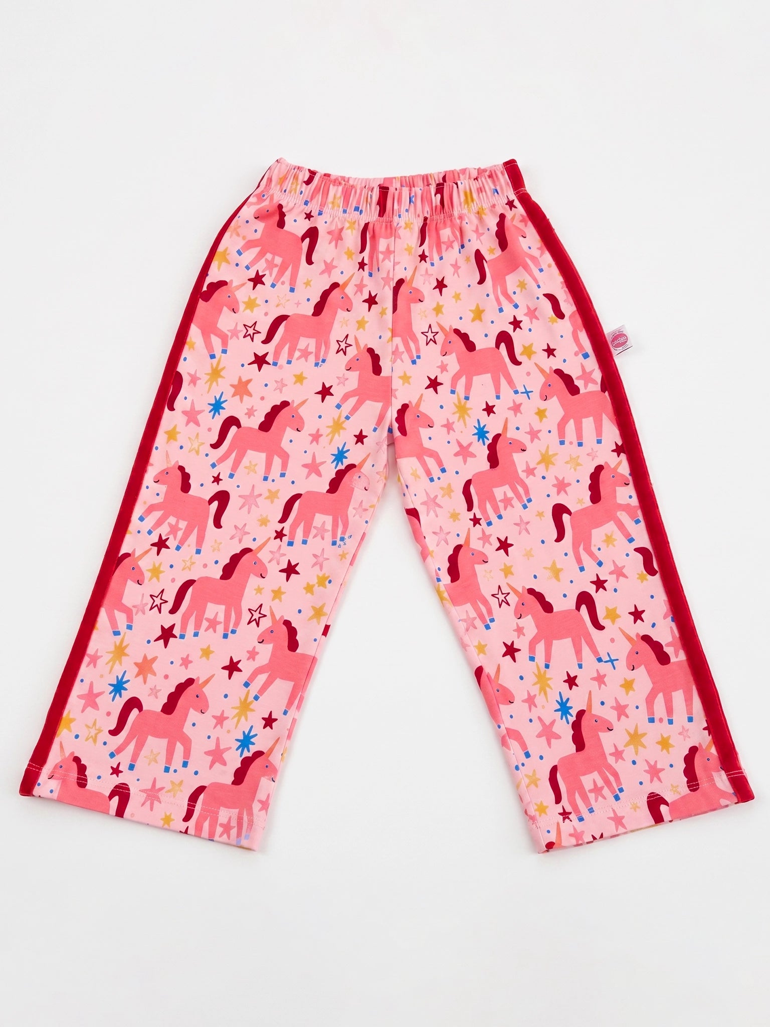 Pink children's pants with an allover unicorn and star print, featuring solid red side panels and elastic waistband, laid flat on a white background.
