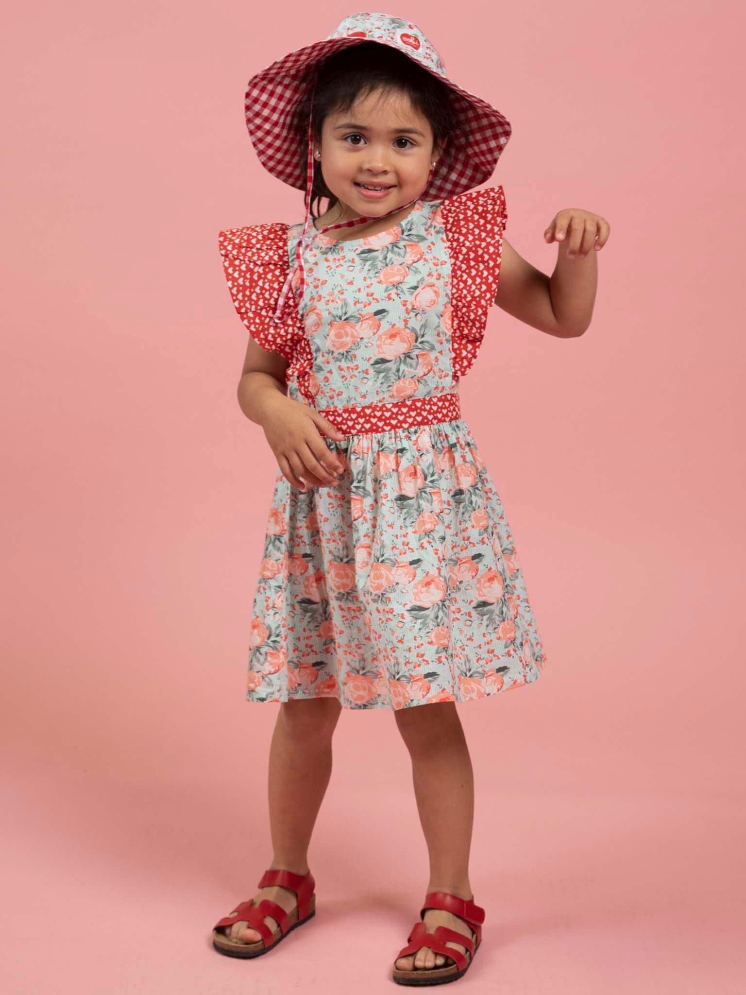 Young girl wearing a vintage roses floral dress and checkered hat on a pink background