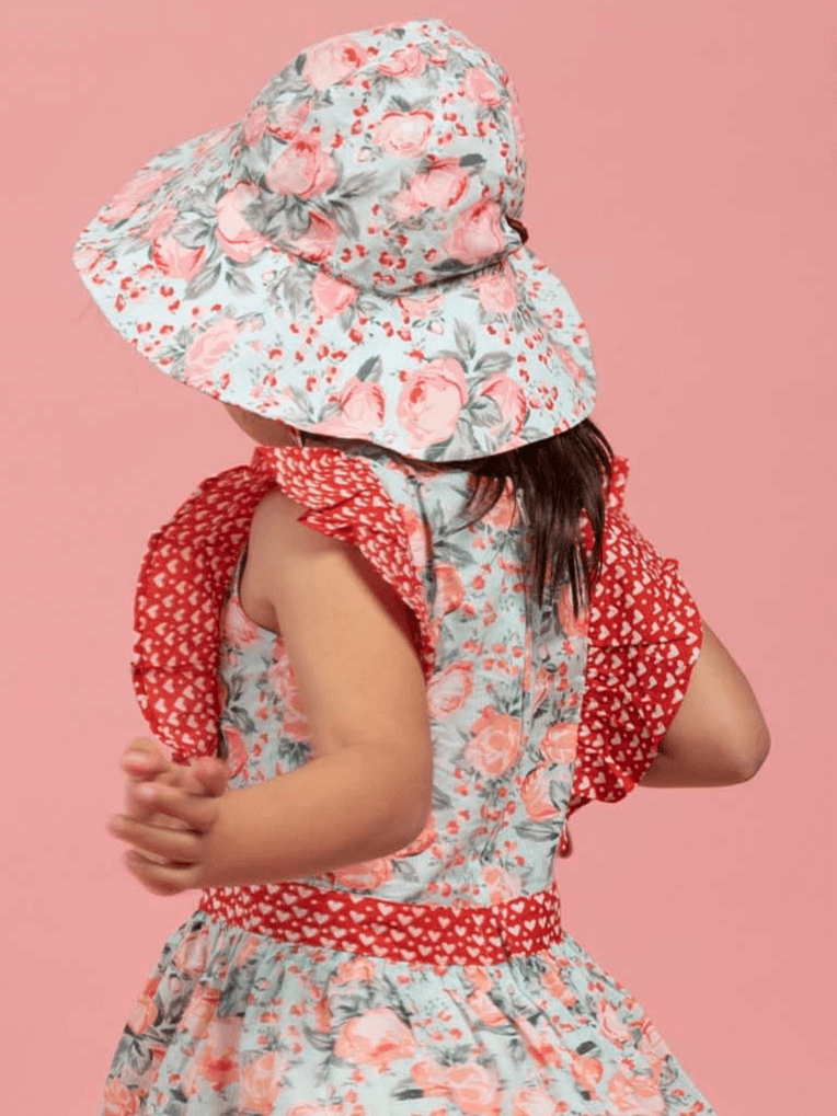 Child wearing a vintage roses floral dress and hat on a pink background