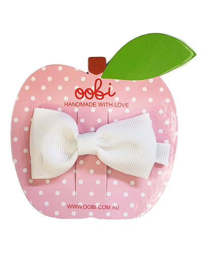 A Essentials Snow White Large Bow hair clip displayed on a pink polka-dotted apple-shaped card labeled "oobi handmade with love.