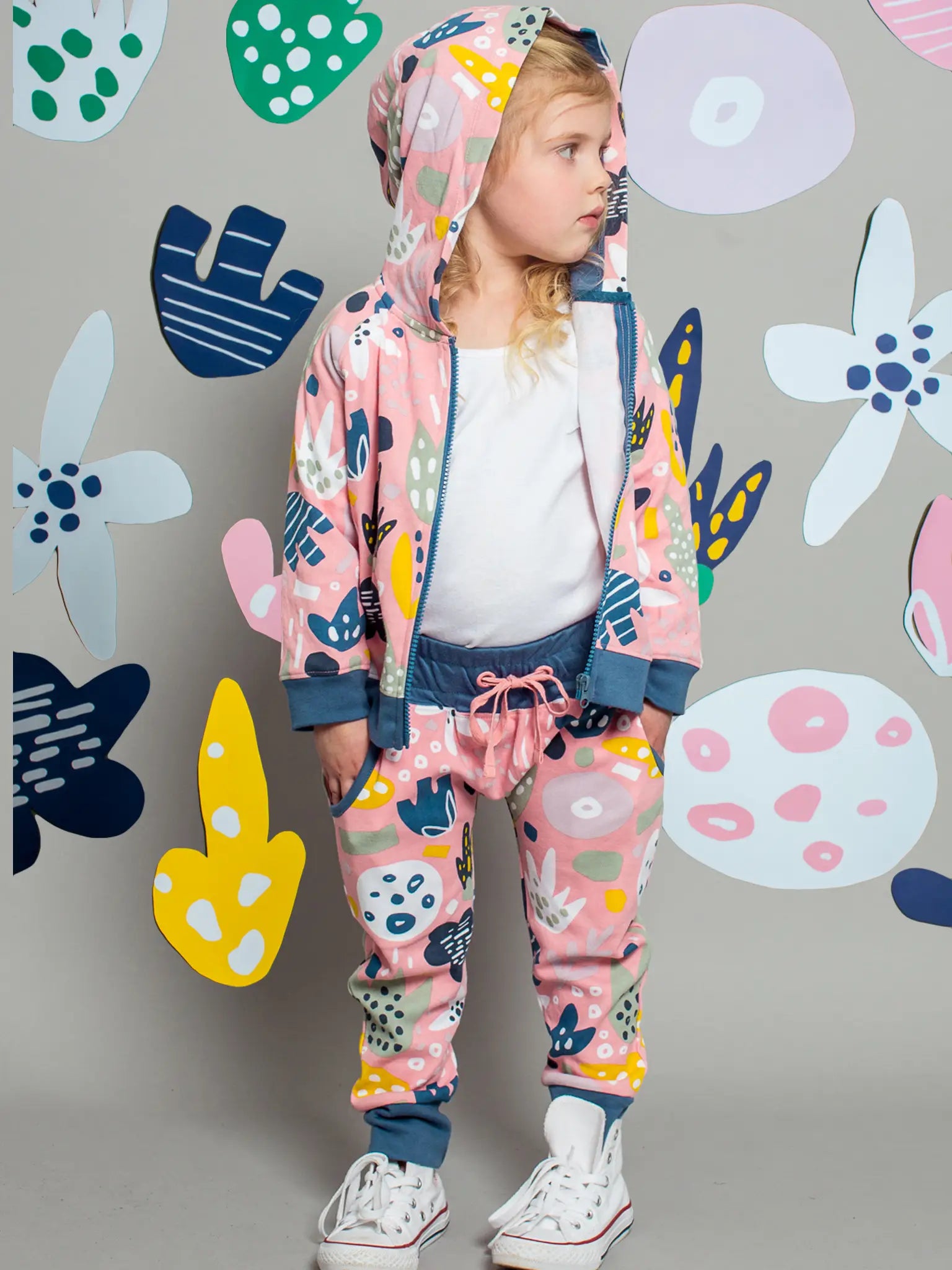 Child wearing a colorful tracksuit with abstract patterns against a floral-patterned wall.
