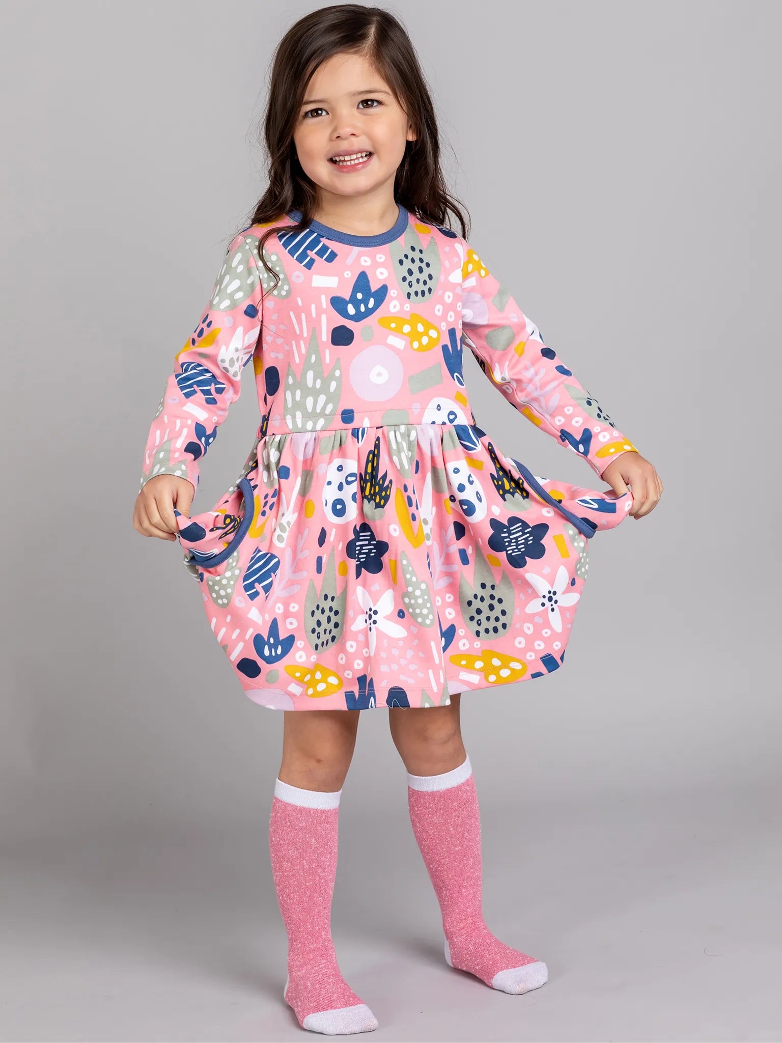 Young girl wearing a colorful dress with long sleeves on a gray background