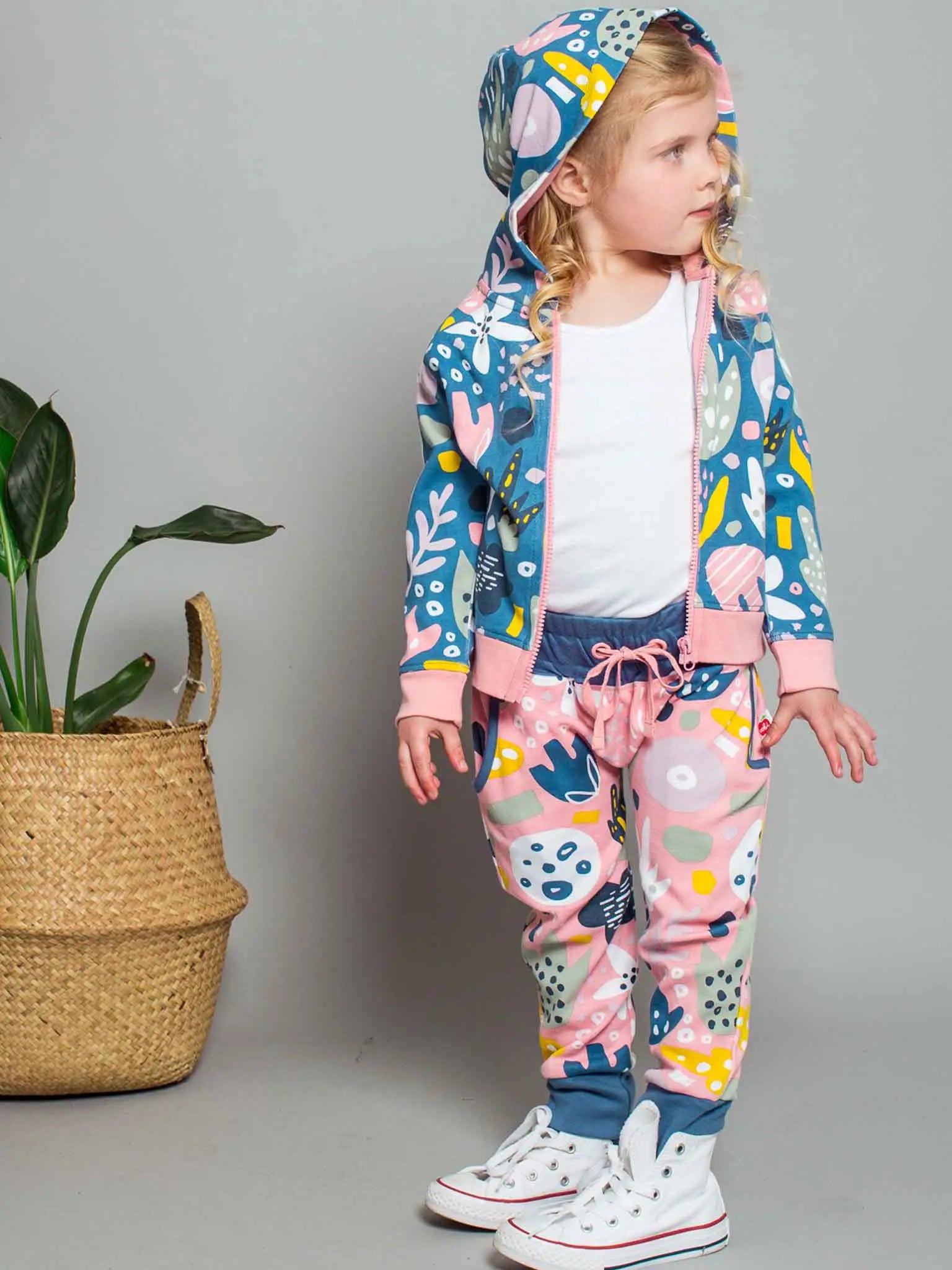 Child wearing a colorful outfit with a patterned jacket and pants, standing against a plain background.