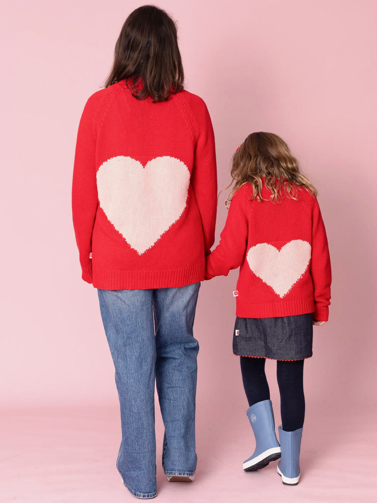 Two people wearing red sweaters with heart designs against a pink background