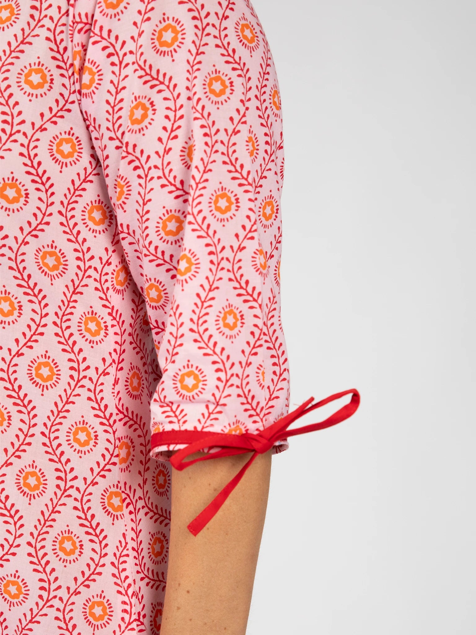 Close-up of a person's arm wearing the Woodblock Women's Resort Dress by Woodblock Flower, featuring a pink and red patterned sleeve with a small red bow at the cuff and a detailed woodblock print.